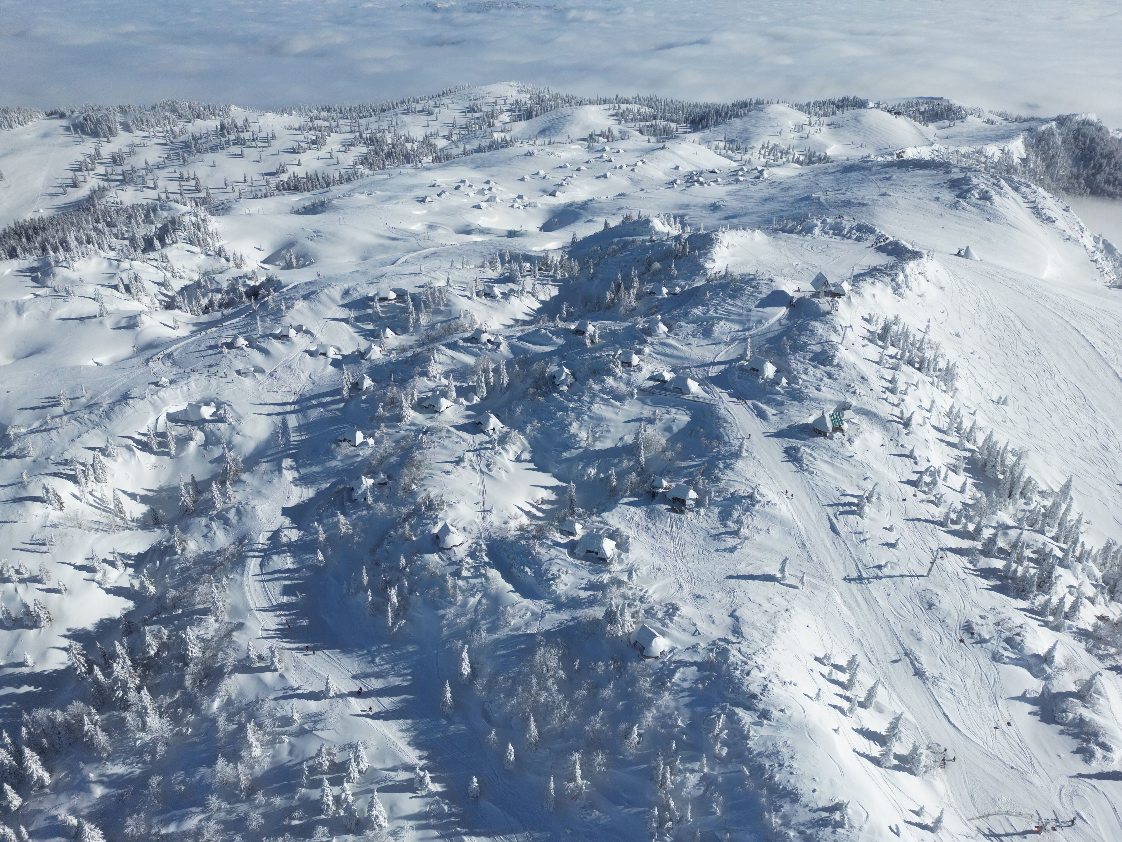 A snow-covered mountainous landscape with ski trails and cabins.