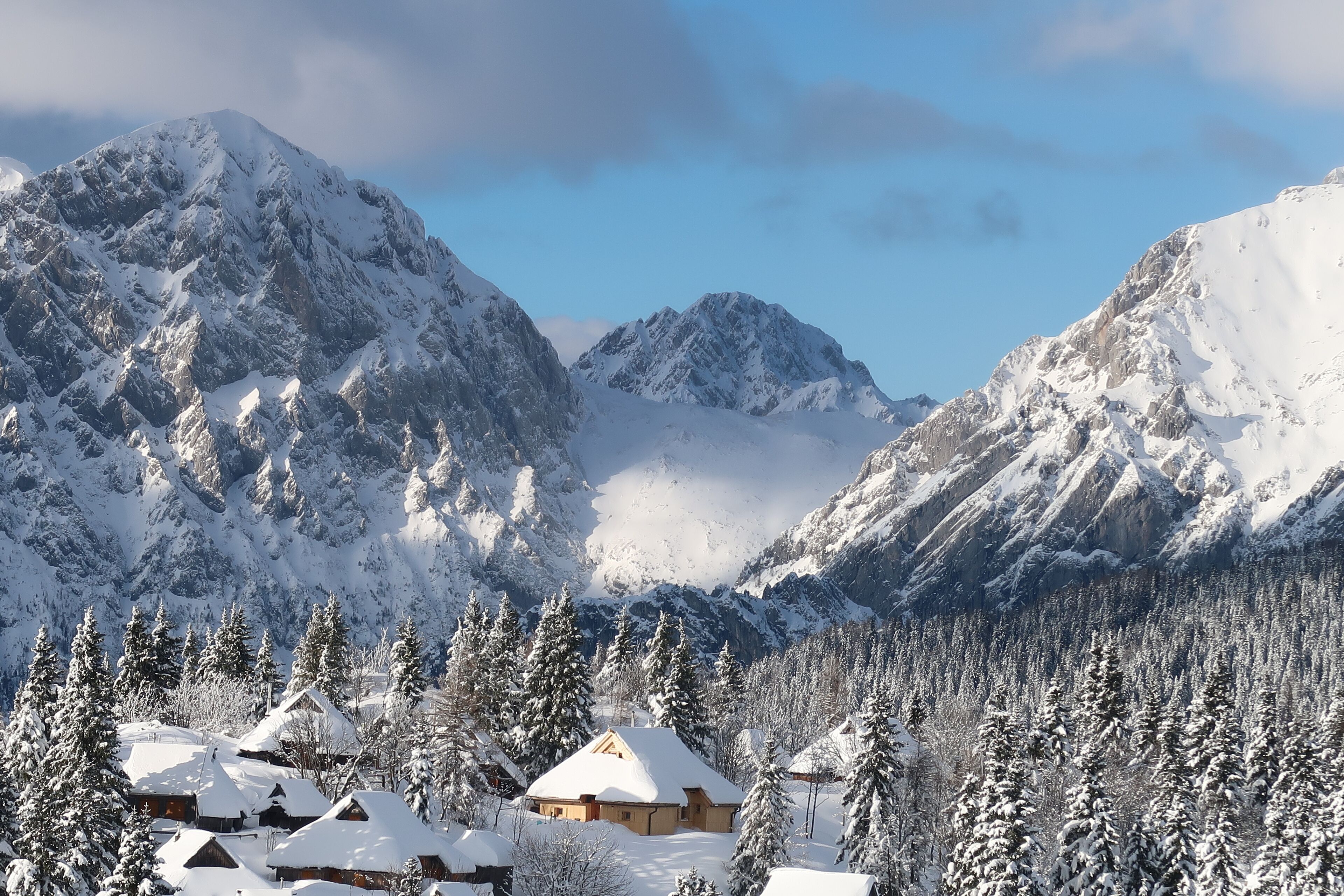 Paisaje montañoso nevado con cabañas de madera y densos árboles de hoja perenne.