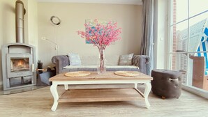 Una sala de estar con chimenea, un conjunto de sofás, una mesa de centro de madera y un jarrón con flores rosas.