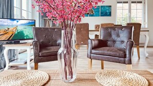 Una sala de estar con dos sillones de cuero marrón, un jarrón transparente con flores rosadas, un televisor y un comedor al fondo.