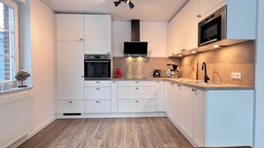 Una cocina moderna con armarios blancos, horno empotrado, microondas y cafetera.