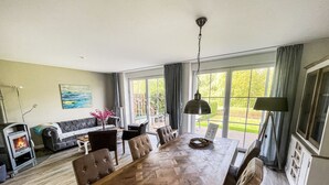 Un salón espacioso con chimenea, un comedor con una larga mesa de madera y grandes ventanales que ofrecen vistas al exterior.