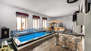 Un salon moderne doté d’une grande piscine, d’un canapé, d’une table basse et d’un coin bar avec des tabourets.