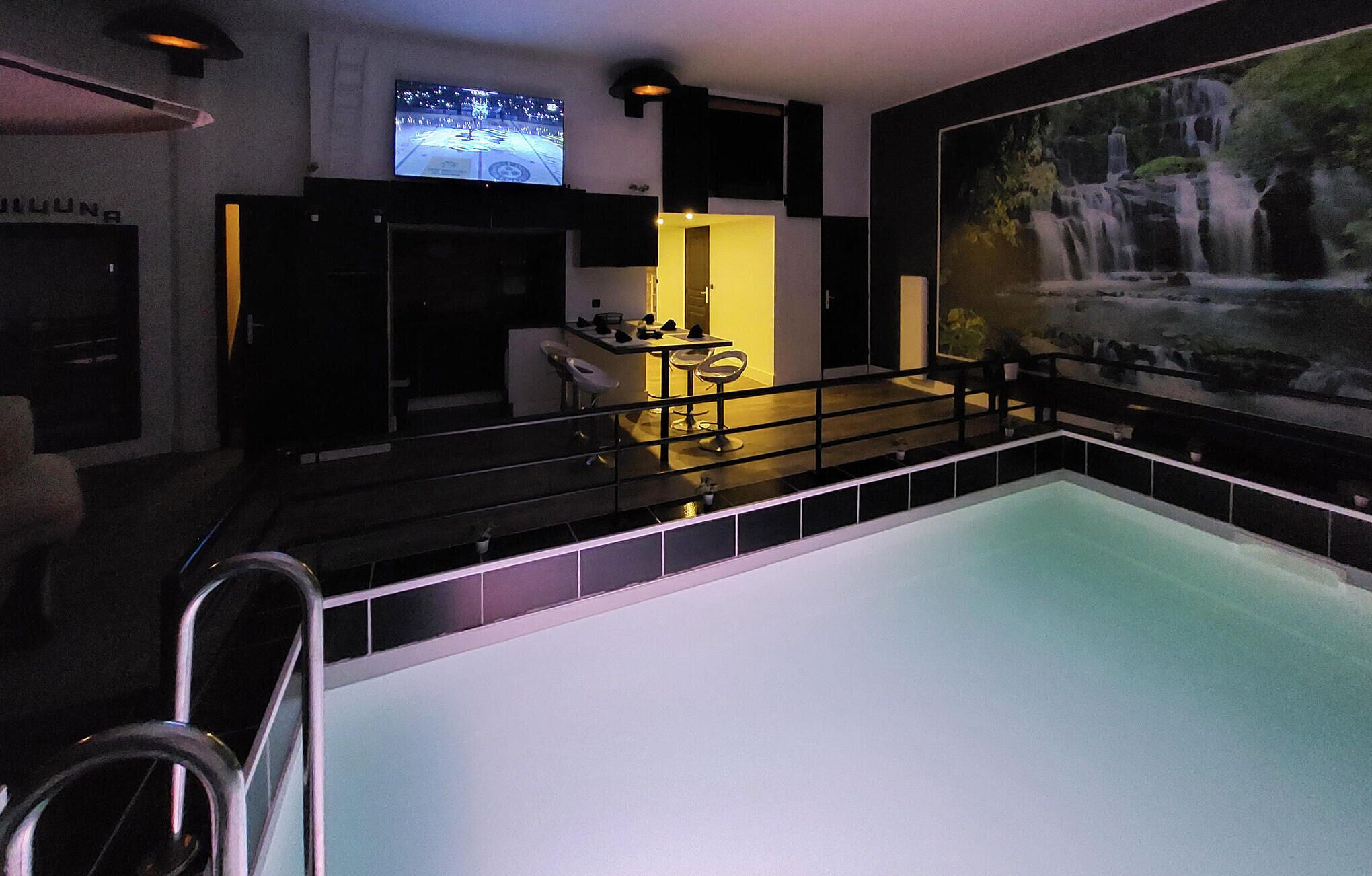 A modern hotel room with a large pool, a bar area, and a waterfall mural.