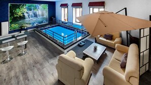 Un salon moderne avec une piscine, des sièges confortables et un grand écran de télévision.
