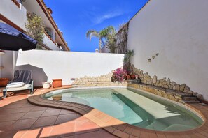 Une piscine à bord incurvé, entourée d’un mur de pierre et agrémentée de plantes en pot.