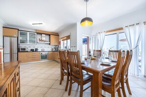 Une cuisine moderne avec des meubles en bois, une table à manger pour quatre personnes et une grande fenêtre agrémentée de rideaux.