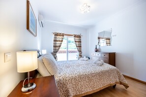 Une chambre à coucher avec un lit, une table de chevet, une lampe et une fenêtre avec des rideaux.