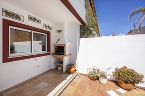 A residential patio with a tiled floor, a window with blinds, a small brick fireplace, and several potted plants.