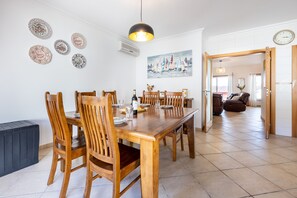 A dining area with a wooden table and chairs, a painting of sailboats, and a clock on the wall. - CoolHouses Algarve Burgau | Casa Boa Vida (Burgau)