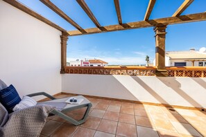 A balcony with a view of buildings, a chair, a table with a book and sunglasses, and a tiled floor. - CoolHouses Algarve Burgau | Casa Boa Vida (Burgau)