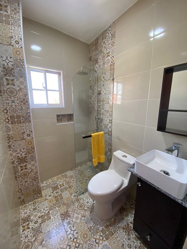 Un baño con ducha, inodoro, lavamanos y ventana.