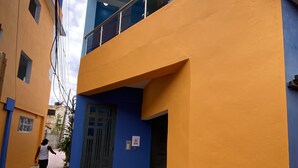 Un bâtiment à la façade bleue et orange, doté d’une entrée fermée par un portail et d’un balcon bien visible.