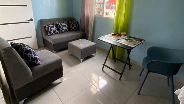 Une petite pièce bien éclairée, avec un canapé, un pouf et une petite table accompagnée d’une chaise.
