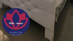 Une chambre à coucher avec un lit doté d’une tête de lit capitonnée, une fenêtre ornée de rideaux à motifs et un appareil de climatisation placé au-dessus de la fenêtre.