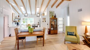 A spacious living area with a wooden dining table, chairs, and a green armchair. A kitchen is visible in the background with modern appliances and a window. - Pet-Friendly Home ~ 6 Mi to Jensen Beach Park! (Jensen Beach)
