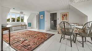 A spacious room with a high ceiling, a dining area with a table and chairs, a large window with a view of greenery, and a blue accent wall. - Stunning home in Vestervig with WiFi (Vestervig)