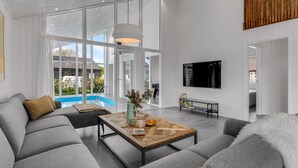 A modern living room with a grey sofa, a wooden coffee table, and a TV mounted on the wall. - Beautiful home in Nexø with kitchen (Nexø)