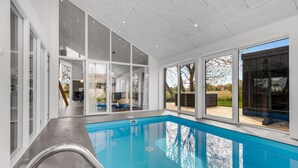 A modern indoor swimming pool with clear glass walls and large windows offering views of the outdoors. - Beautiful home in Nexø with kitchen (Nexø)