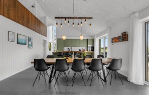 Enjoy meals in this stylish dining area with a long table and pendant lights, surrounded by framed artwork and a large window offering a view of the outdoors.