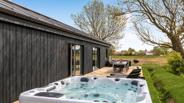 A modern outdoor hot tub area with a wooden deck and a dining table. - Beautiful home in Nexø with kitchen (Nexø)