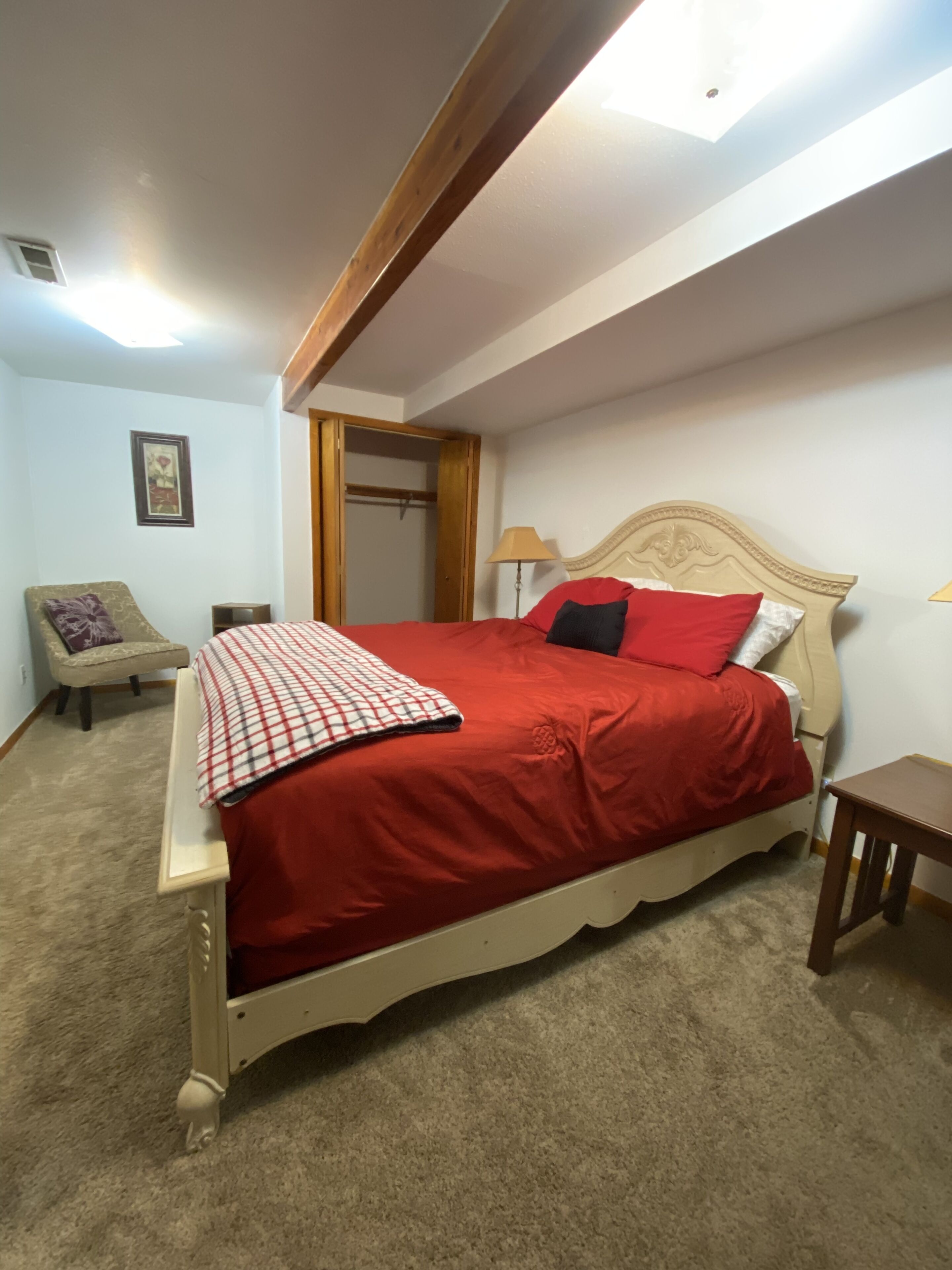 Un dormitorio con cama, una silla, mesita de noche, lámpara y armario.