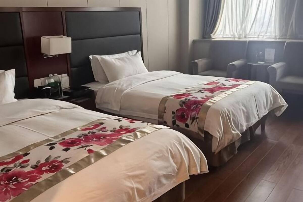 Habitación de hotel con dos camas, una mesita de noche, una lámpara, una pequeña mesa y una ventana con cortinas.
