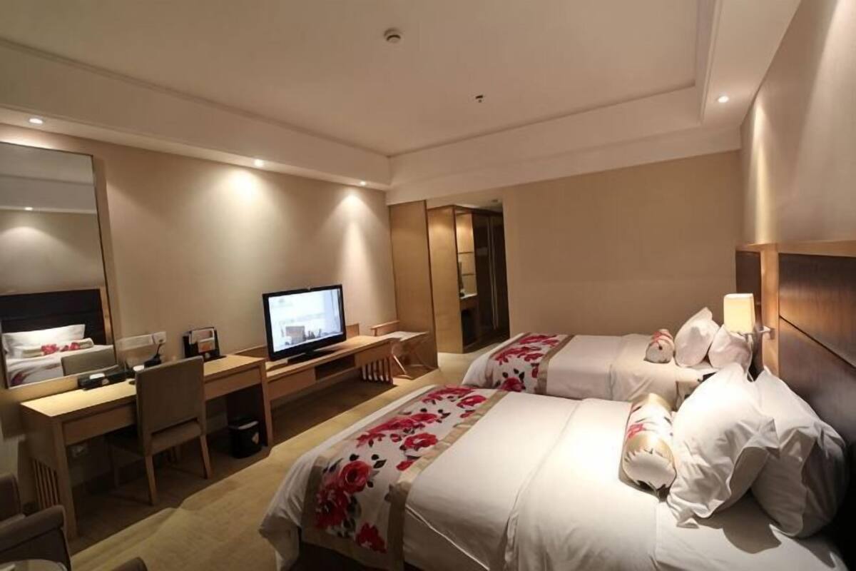 Habitación de hotel con dos camas, un escritorio con computadora, televisión y espejo.