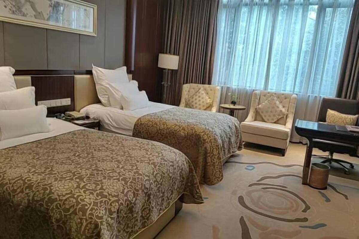 Habitación de hotel con dos camas, un escritorio, una silla, una lámpara y vistas al exterior.