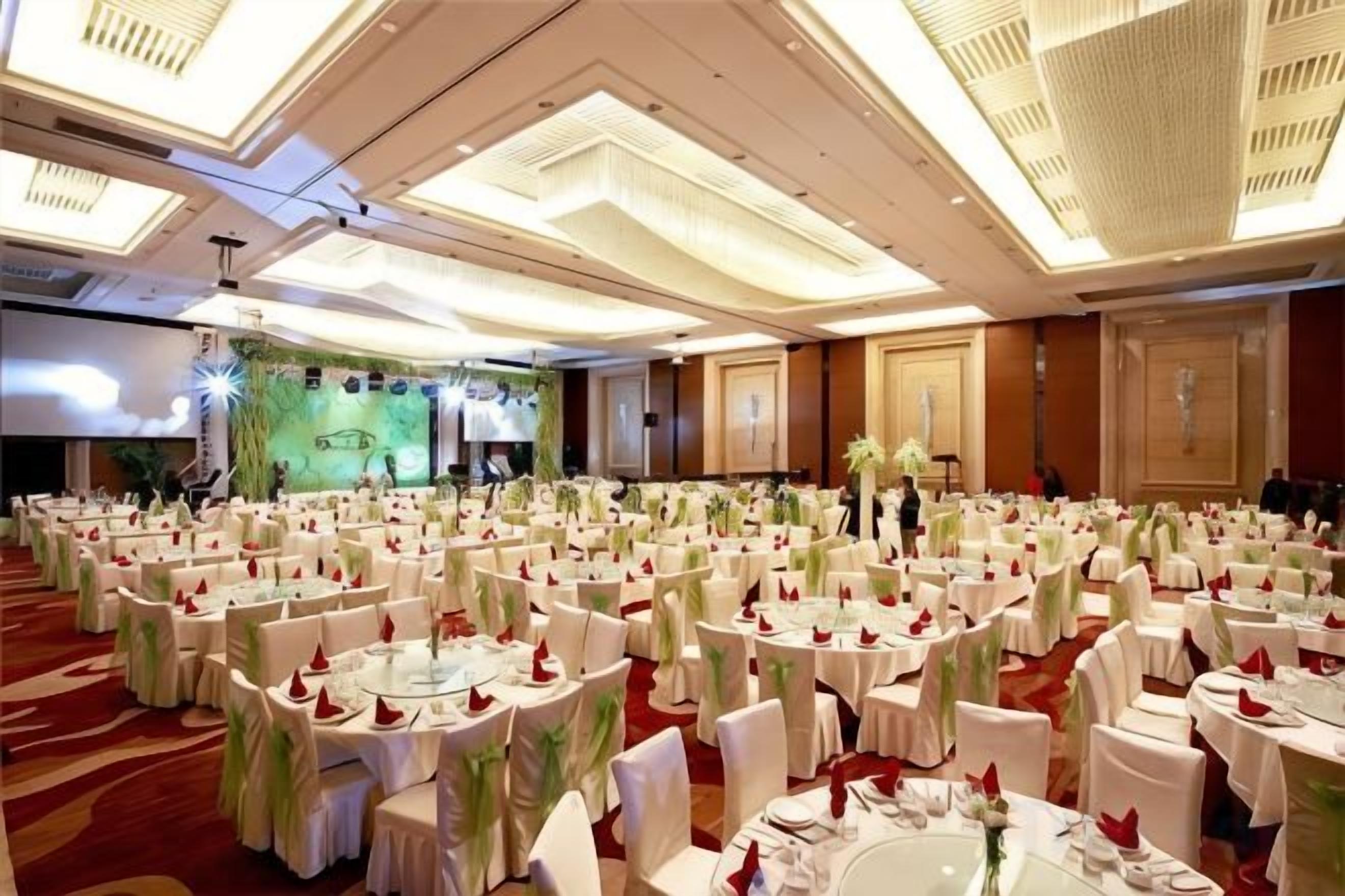 A banquet hall with round tables, chairs, and a stage with a screen.