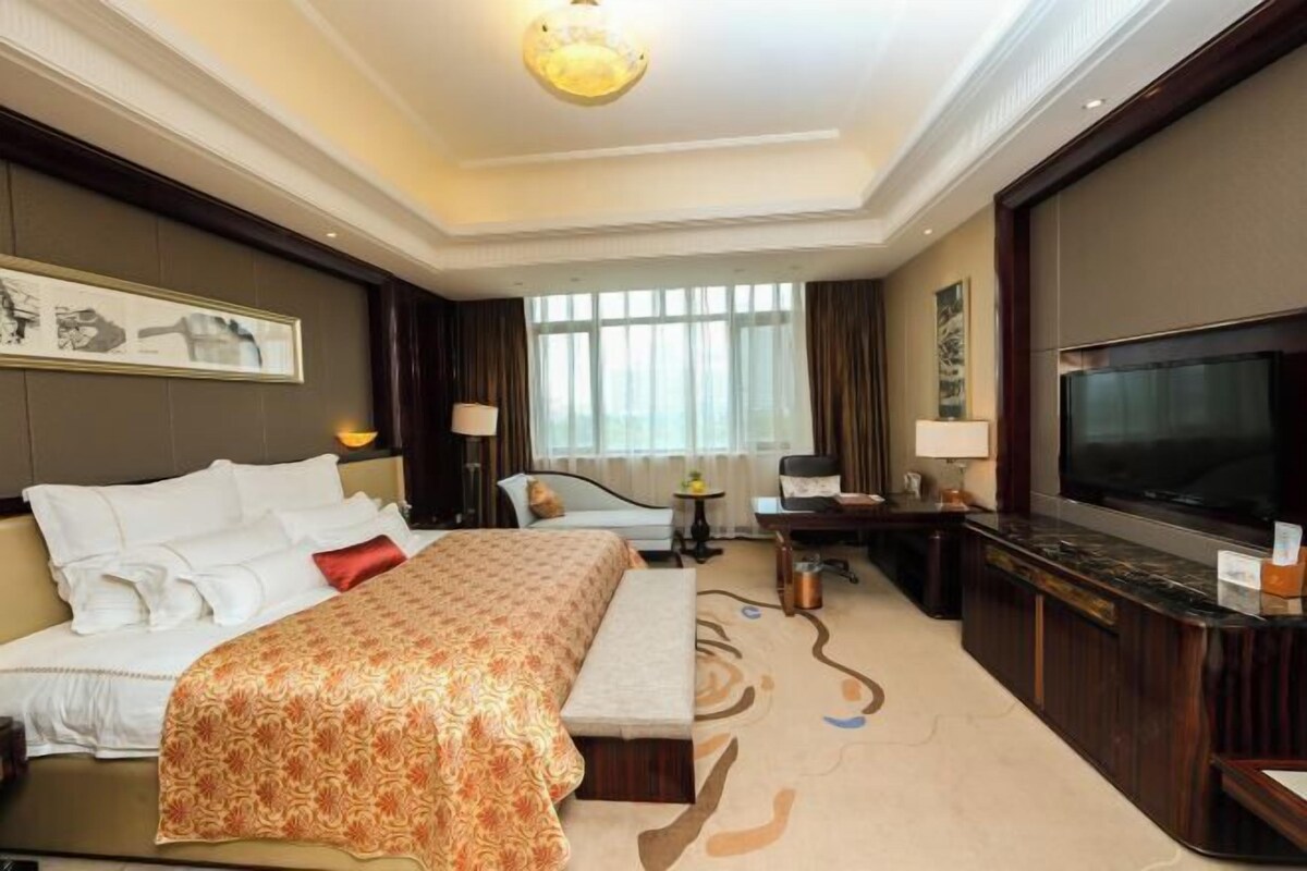 A hotel room with a large bed, a desk, a television, and a view of the outdoors.