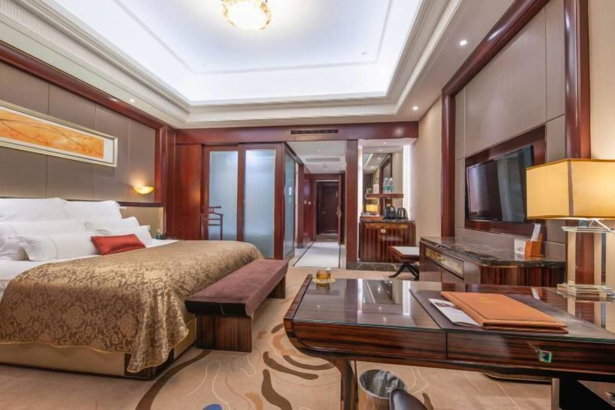 Habitación de hotel con una cama grande, un escritorio, televisión y un baño visible a través de una puerta abierta.