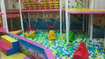Un área de juegos infantiles con piscina de pelotas, columpios y una estructura para escalar.