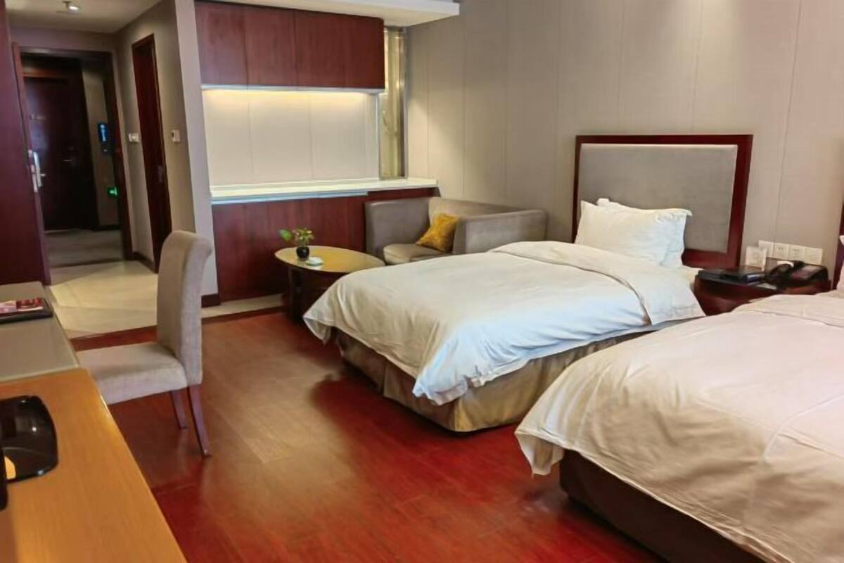 Una habitación de hotel con cama, escritorio, silla, mesita con planta y ventana.