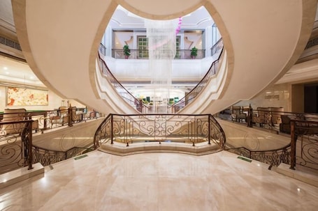 A spacious atrium with a central water feature, multiple floors, and ornate railings.. Mingdu Hotel