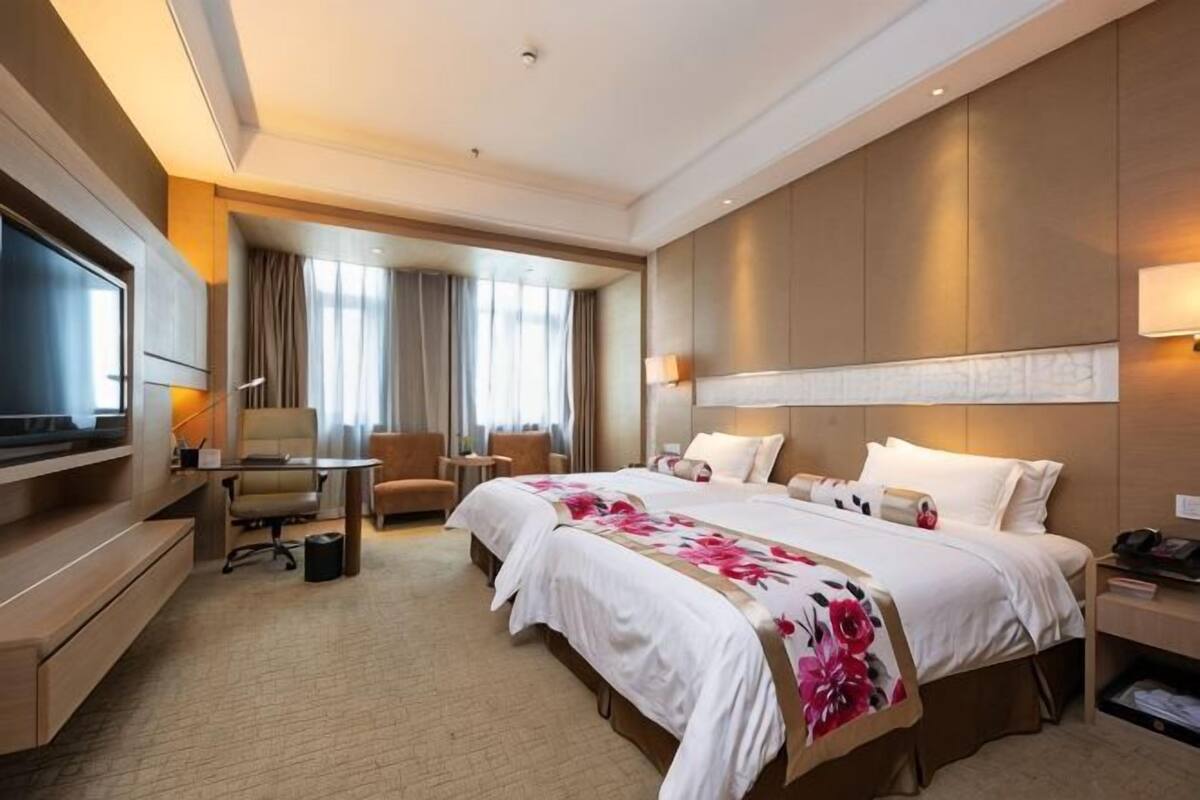 Habitación de hotel con una cama grande, un escritorio, una silla, un televisor y una ventana con cortinas.