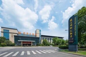 A hotel entrance with a large sign, a clear sky, and a parking lot. - Mingdu Hotel (Zhenjiang)
