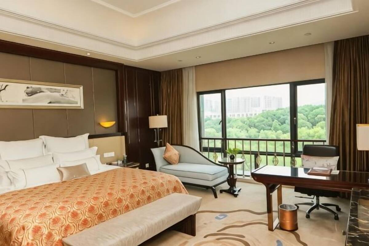 Habitación de hotel con una cama grande, un escritorio, una silla y vistas a zonas verdes por la ventana.