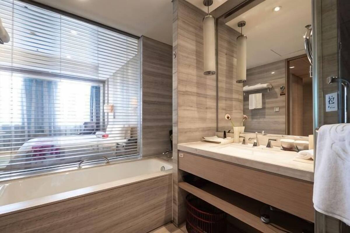 Un baño moderno con bañera, un espejo grande y una ventana con persianas.