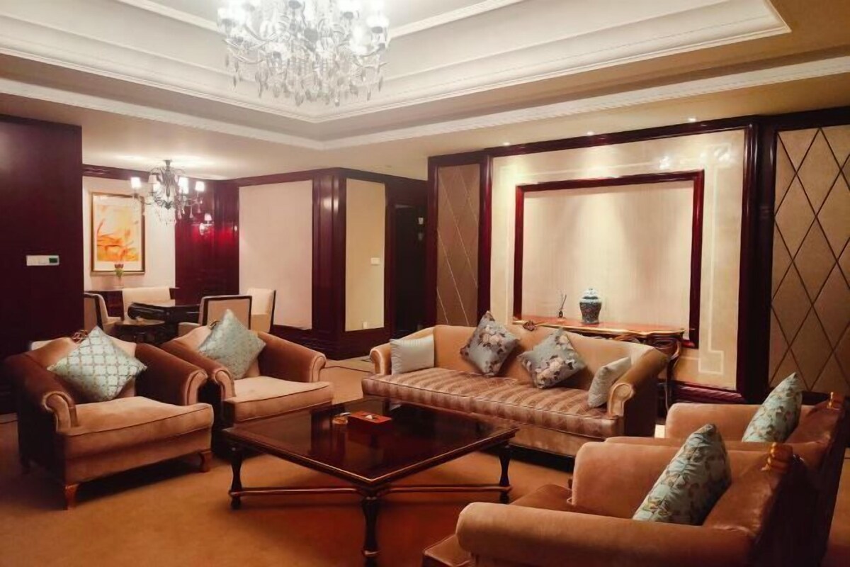A spacious living room with leather sofas, a coffee table, and a chandelier.