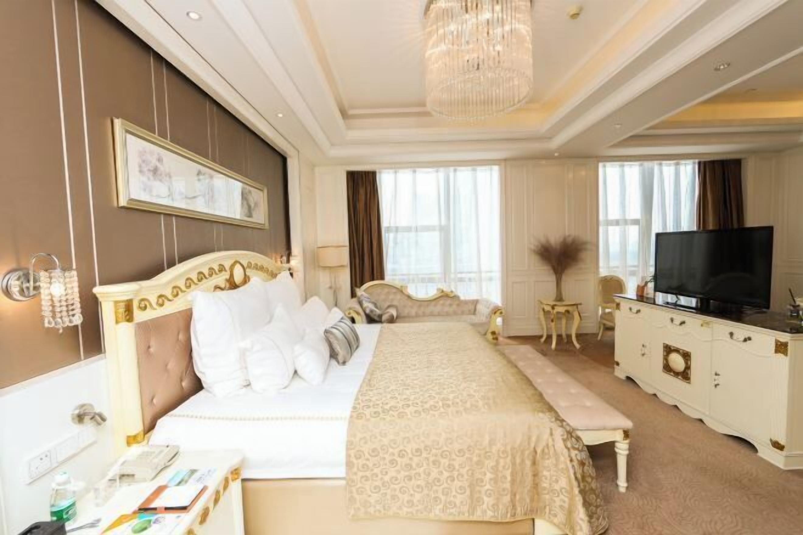 Una habitación de hotel con una cama grande, televisor, escritorio con teléfono y una araña.