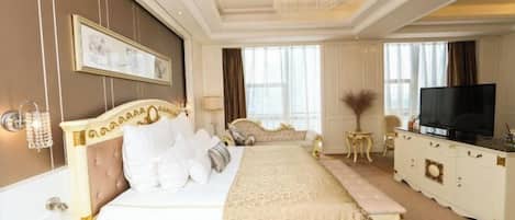 A hotel room with a large bed, a television, a desk with a telephone, and a chandelier.