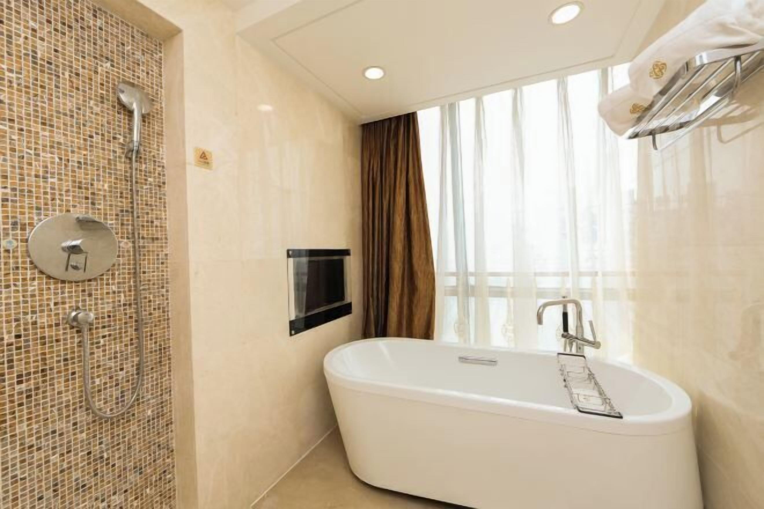 A modern bathroom with a freestanding bathtub, a shower area with a mosaic wall, and a large window with curtains.