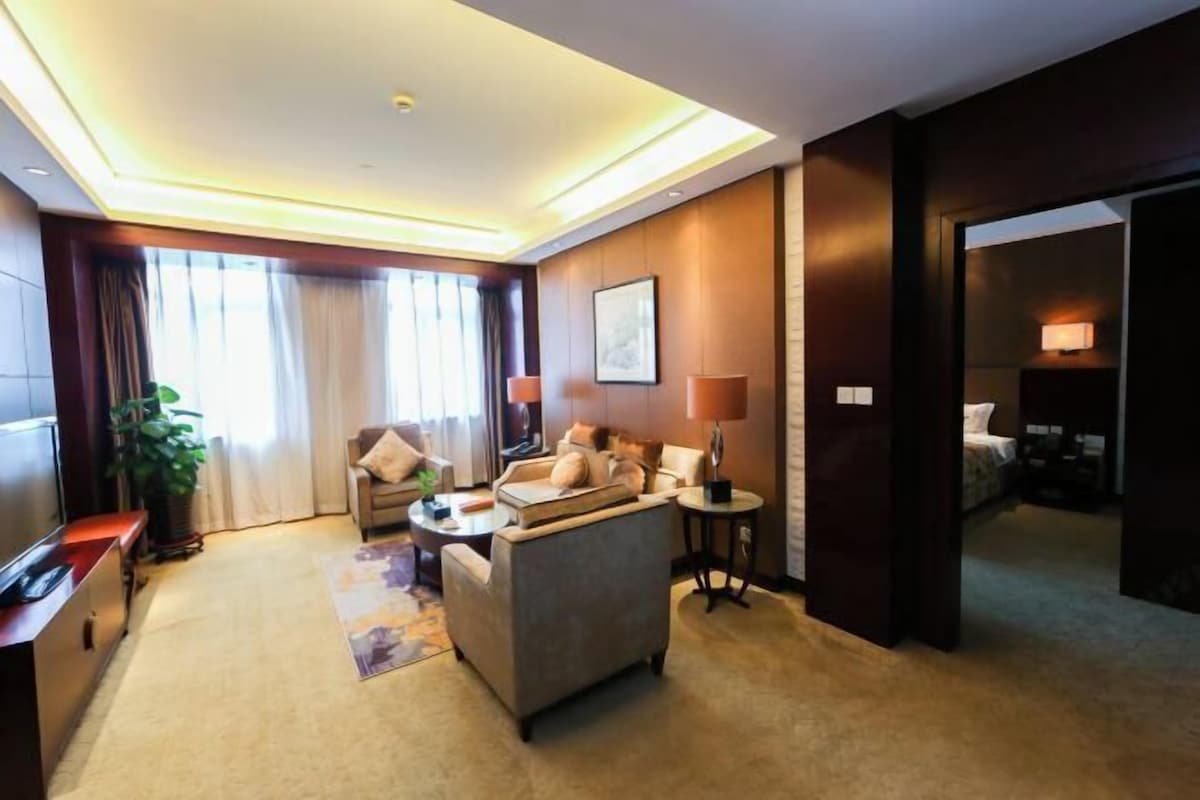 A hotel room with a sofa, armchair, coffee table, TV, and a small side table.