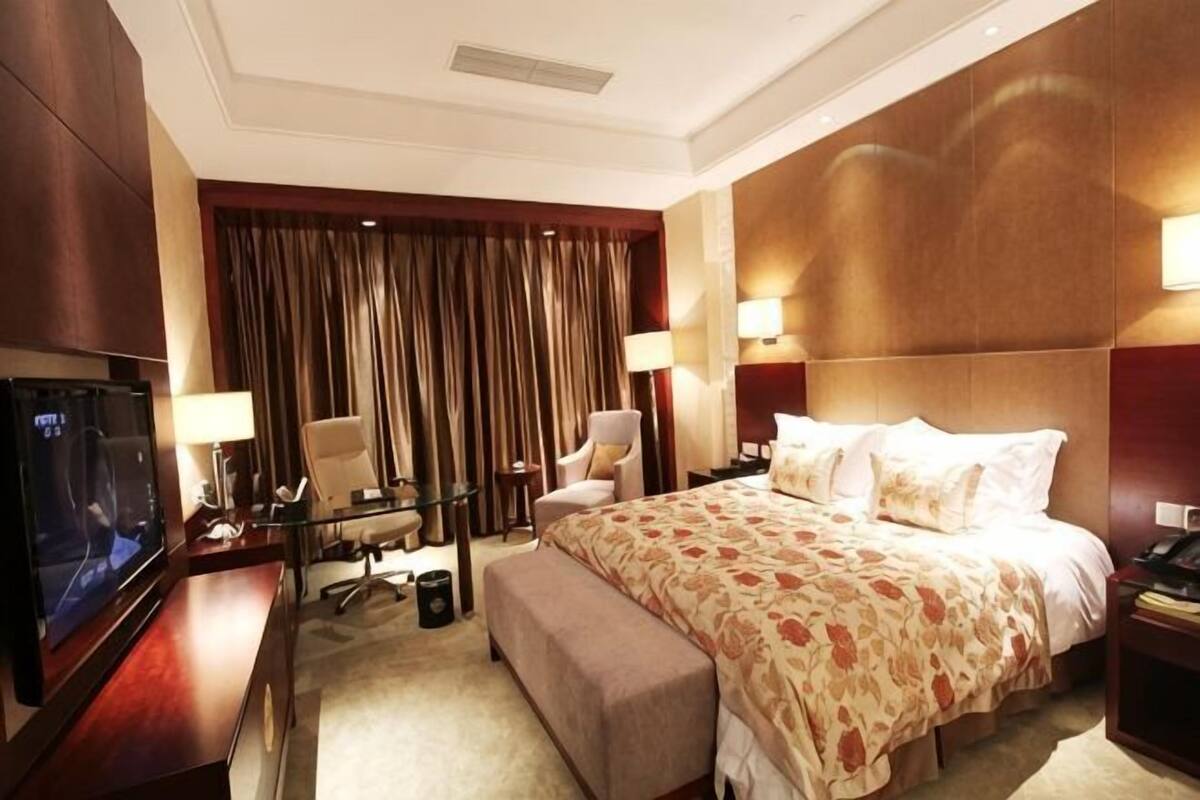 Habitación de hotel con una cama grande, televisor, escritorio con silla y ventana con cortinas.