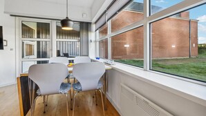 A modern kitchen with a dining area, large windows, and a view of a brick building. - 2 bedroom awesome apartment in Fanø (Fanø)