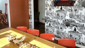 A dining area with a long wooden table, red chairs, and a wall with a cactus-themed mural.