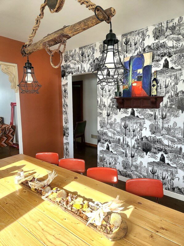 Un comedor con una larga mesa de madera, sillas rojas y un mural con motivos de cactus.