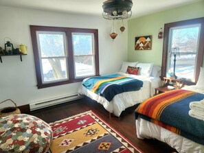 Un dormitorio acogedor con dos camas, un ventanal grande, una lámpara colgante y una alfombra.