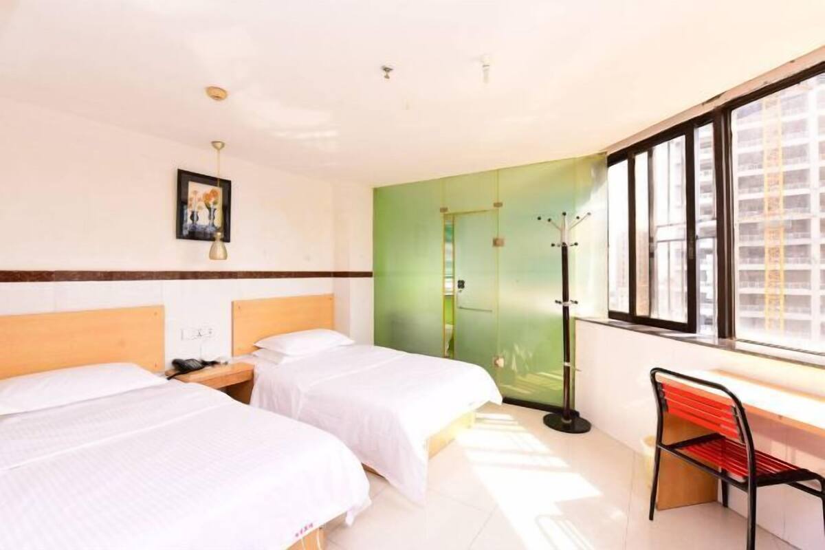Habitación de hotel con dos camas, un escritorio, una silla, una puerta verde y una ventana con persianas.